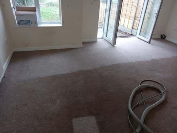 This is a photo of an empty living room with a brown carpet that is in the process of having its carpets steam cleaned