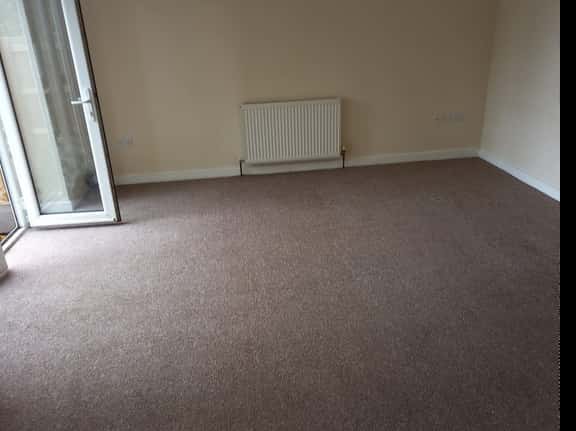 This is a photo of a living room after it has been cleaned. The room is empty and has a brown carpet that has been steam cleaned
